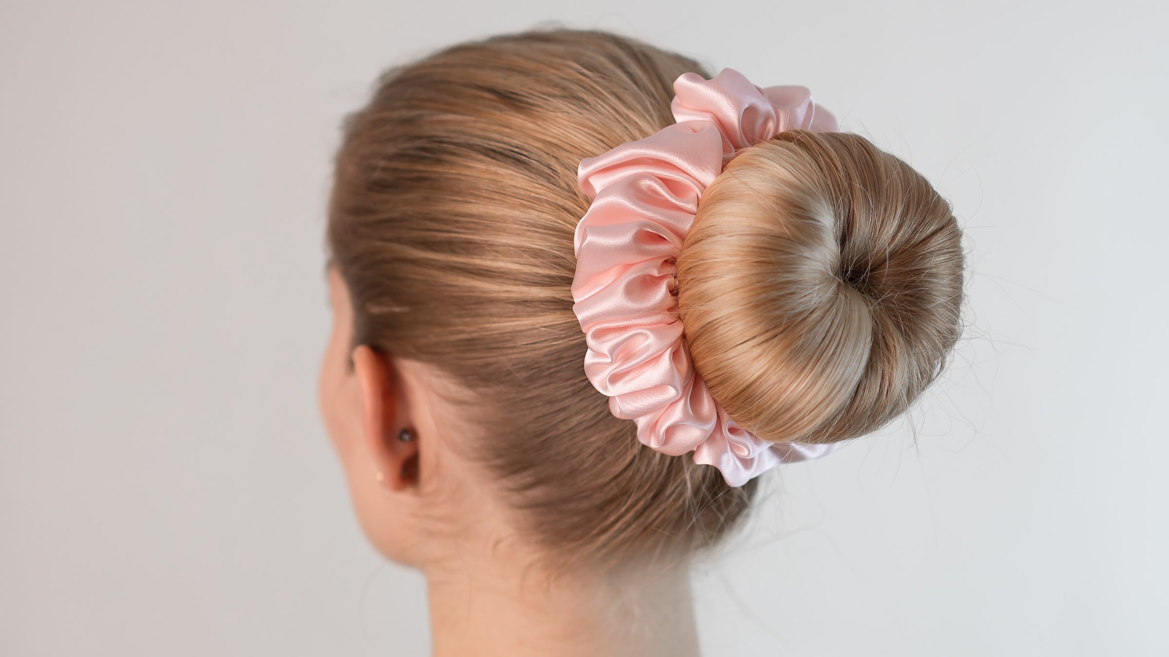 Schöne Frau mit langen blonden Haaren trägt einen rosa Seiden Scrunchie von Curly N Covered im Haar
