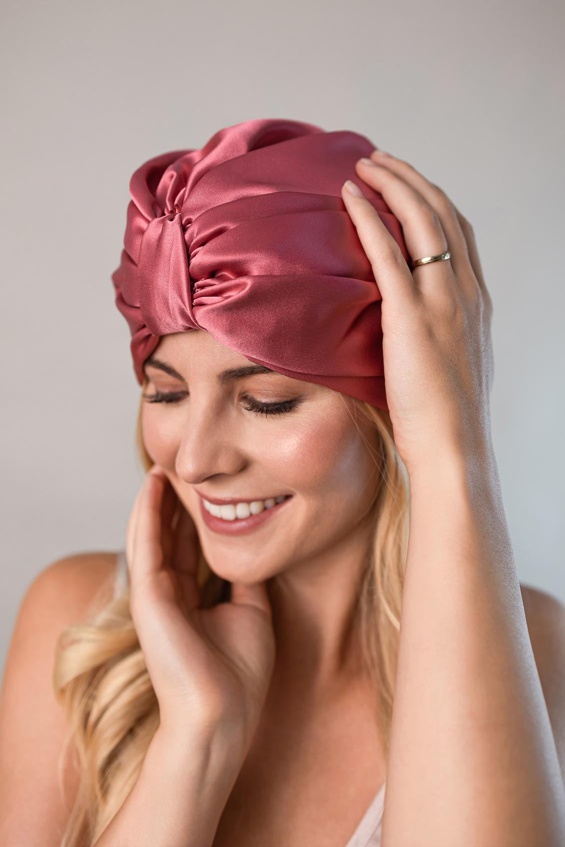 Wunderschöne Frau mit langen blonden Haaren trägt einen Seidenturban aus reiner Maulbeerseide in dunkel rosa von CURLY N COVERED zum Schutz ihrer Haare 