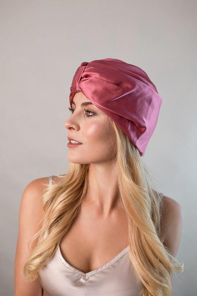Schöne Frau mit langen blonden Haaren trägt einen Seidenturban aus edler Maulbeerseide in dunkel rosa von CURLY N COVERED zum Schutz ihrer Haare 