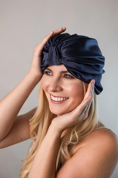 Schöne Frau mit langen blonden Haaren trägt einen Seidenturban aus reiner Maulbeerseide in marine blau von CURLY N COVERED zum Schutz ihrer Haare