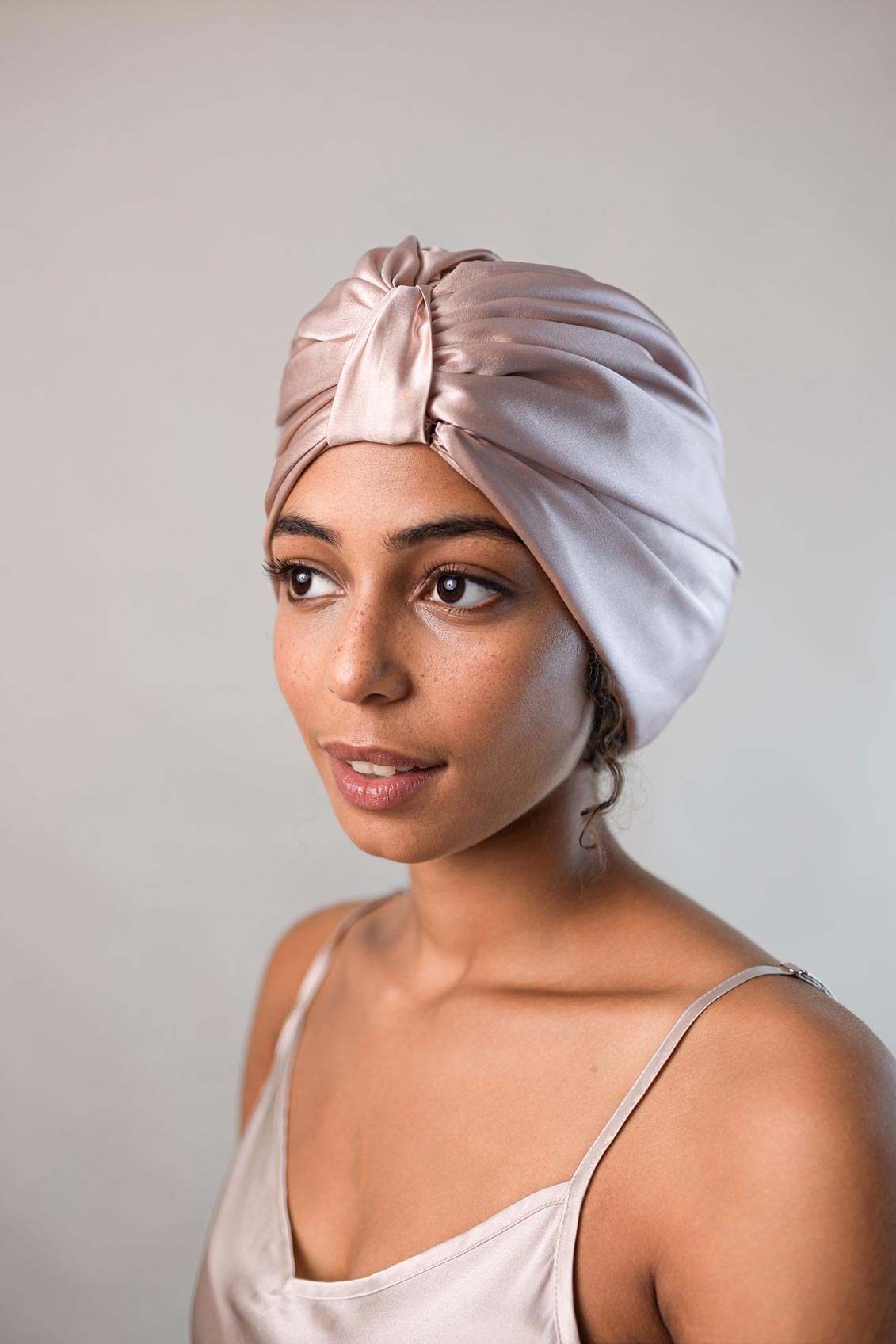 Schöne Frau mit dunklen lockigen Haaren trägt einen sand-farbene Schlafhaube aus reiner Maulbeerseide von CURLY N COVERED zum Schutz ihrer Locken