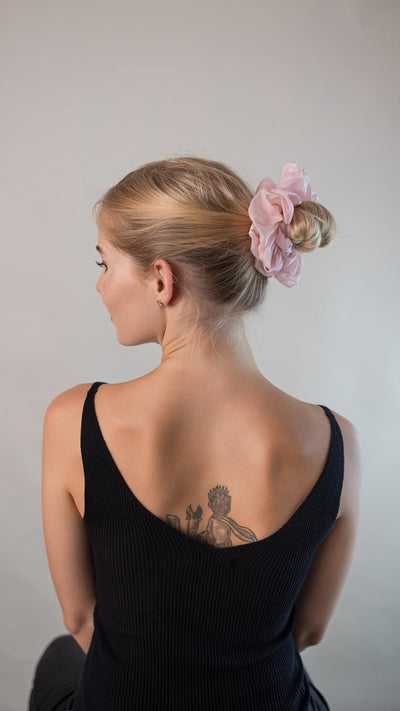 Schöne Frau mit blonden Haaren trägt einen blass rosa XXL Scrunchie aus Cotton Silk (Baumwolle und Seide) von Curly N Covered im Haar.