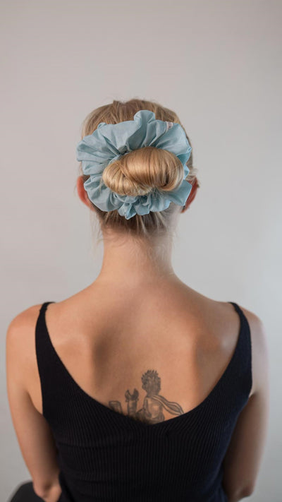 Wunderschöne Frau mit blonden Haaren trägt einen hell blauen XXL Scrunchie aus Cotton Silk (Baumwolle und Seide) von Curly N Covered im Haar.